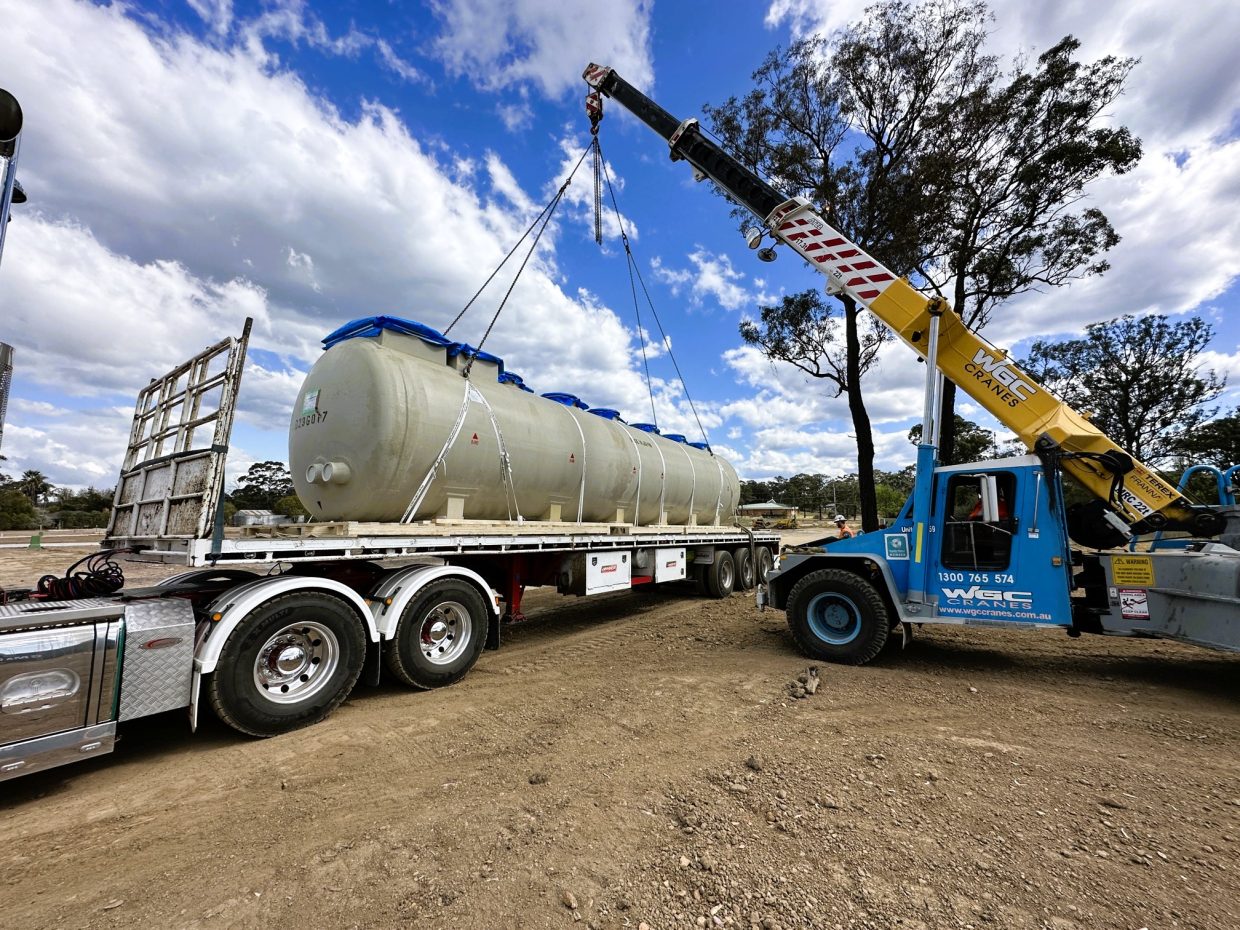 Pre manufactured Kubota wastewater treatment tank being lifted by a crane from a flatbed truck.