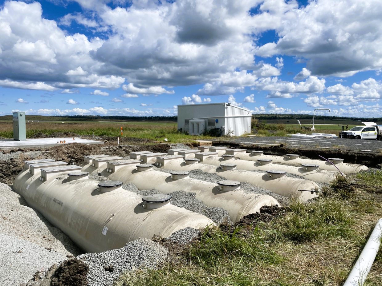 Wastewater treatment tanks are installed, building and a vehicle in the background.