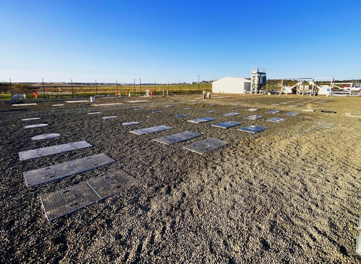 Several metallic manhole covers laid out on gravel.