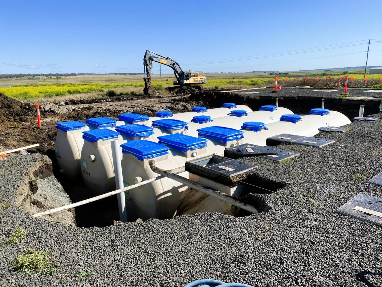 Wastewater treatment tanks with blue lids is partially buried in a trench at a construction site.