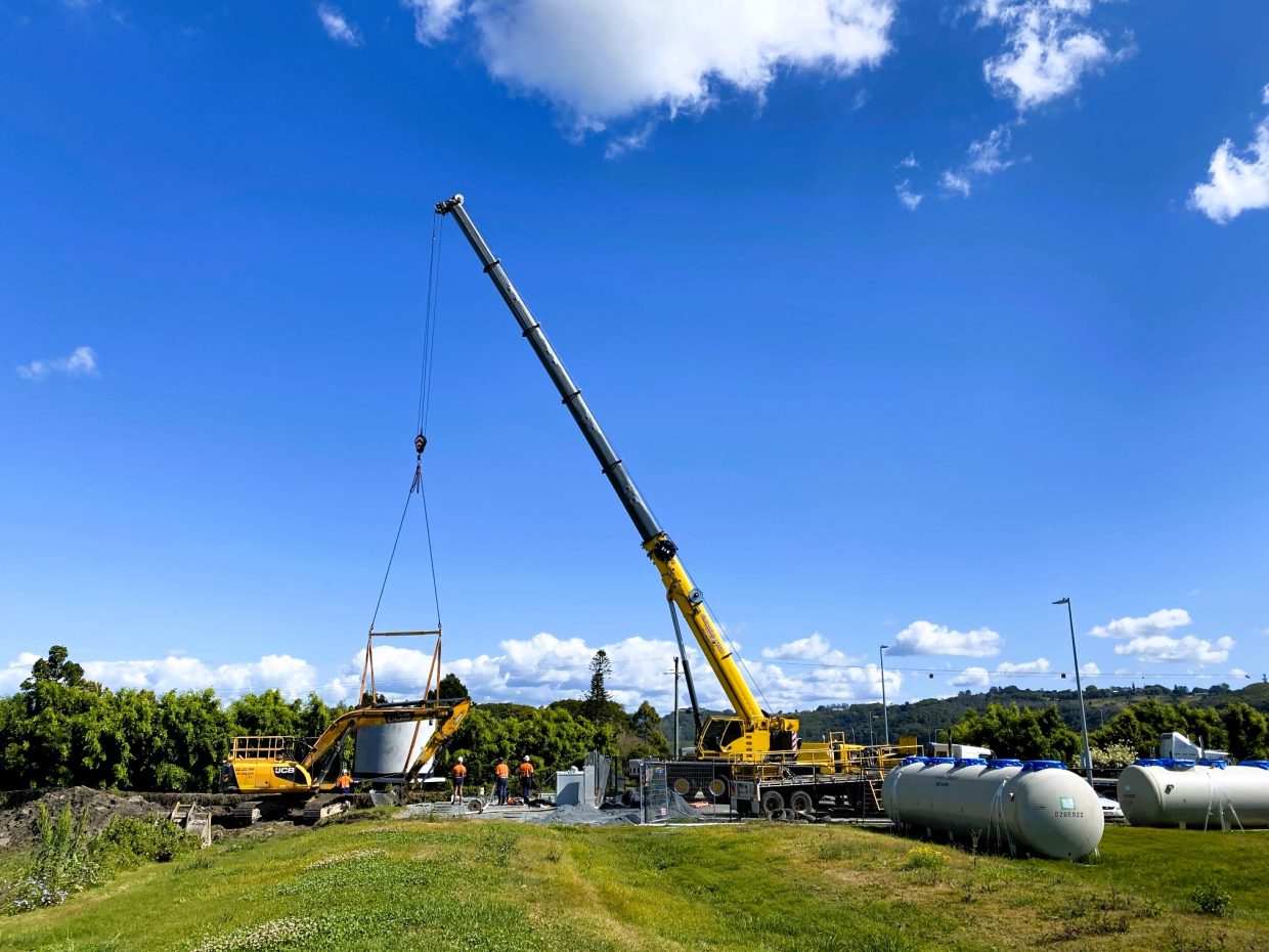 Crane hoists a large concrete tank.